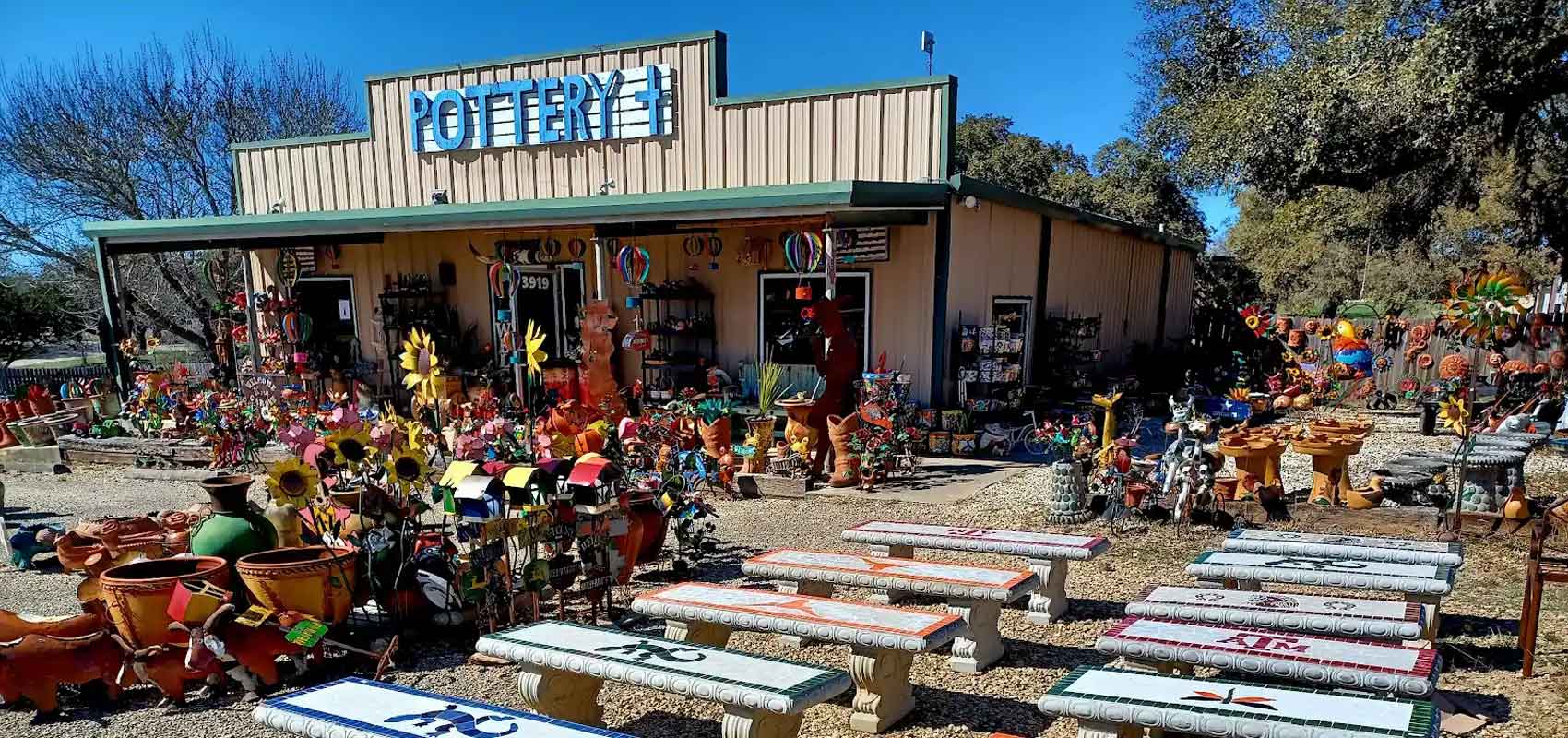The storefront of Pottery Plus, with rows of benches and garden art in front