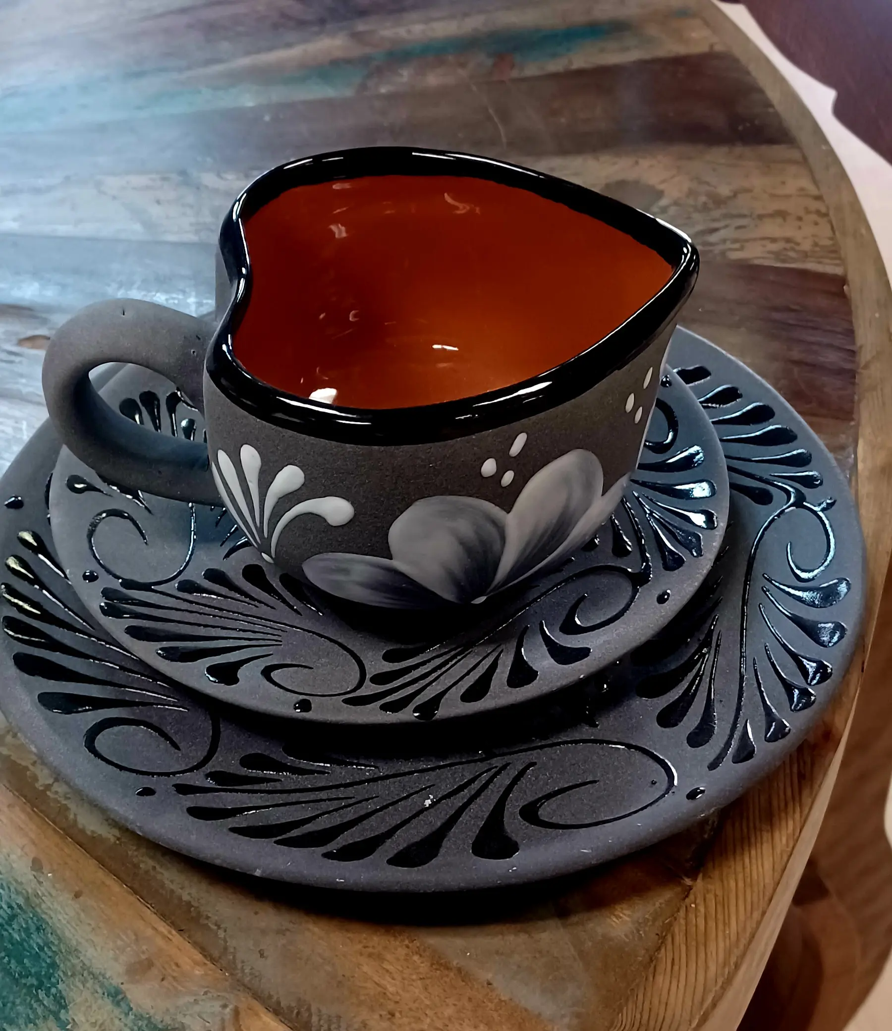 A grey teacup with a red interior on two grey dishes with floral designs